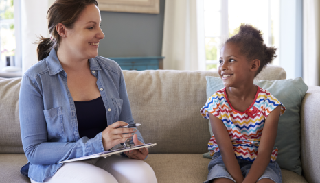 woman with a clipboard talking to a child on a couch